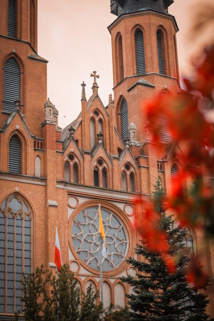 Stunning gothic cathedral facade adorned with vibrant red foliage and national flags, vertical perspective.