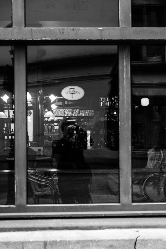 Moody black and white reflection of a cafe interior through a window.
